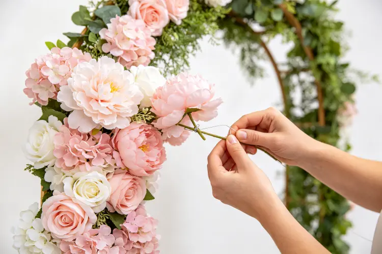 Adding artificial flowers to arch frame with floral wire and hot glue