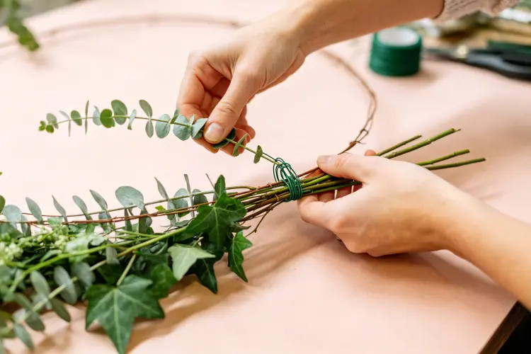 Adding greenery base layer to DIY flower garland showing wire wrapping technique