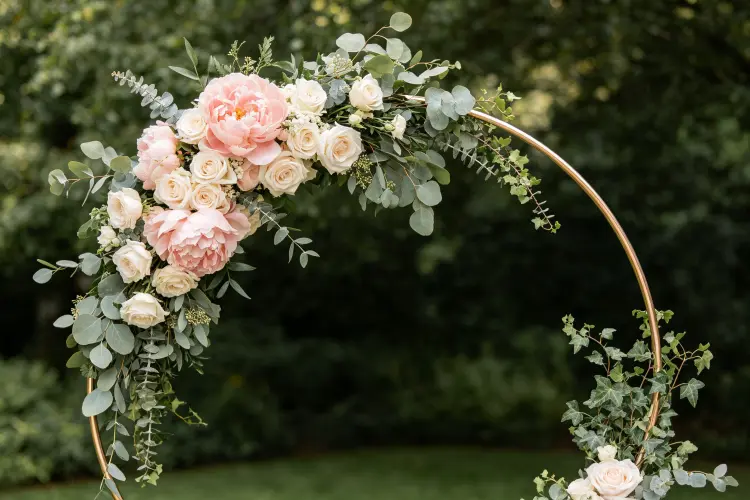Asymmetric floral hoop with flowers concentrated on one side and trailing greenery, blush and sage color palette