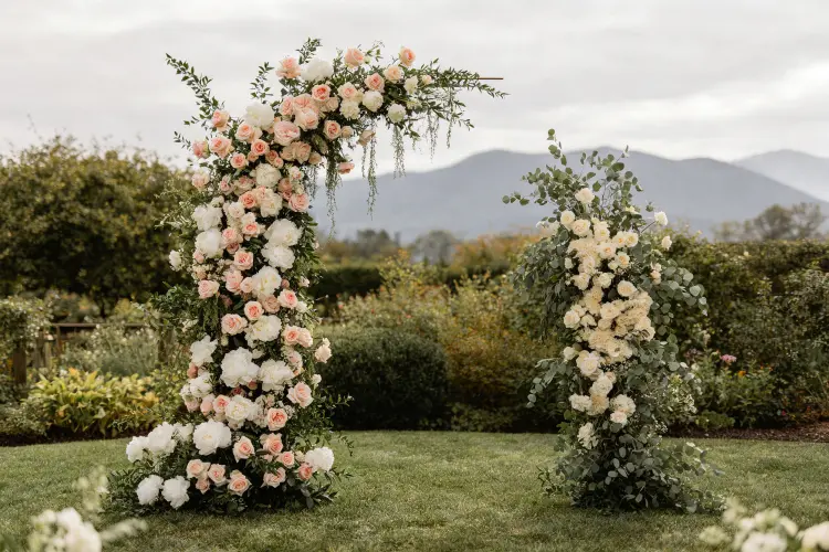 Broken arch wedding ceremony with two asymmetrical floral pillars at outdoor garden venue