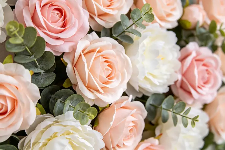 Close-up detail of artificial flower wall panel with roses, peonies, and eucalyptus greenery, showing petal texture and color variation for rental inventory